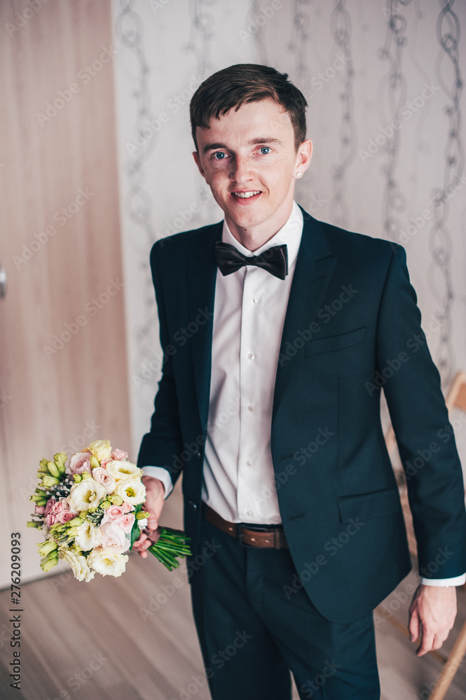Happy groom standing and pose. wedding morning. close up. background. Smile, portrait. Wedding bouquet of roses Happy groom standing and pose. wedding morning. close up. background. Smile, portrait. Wedding bouquet of roses
