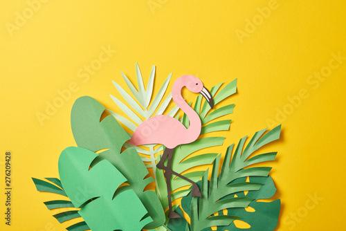 top view of paper cut green palm leaves and pink flamingo on yellow background with copy space