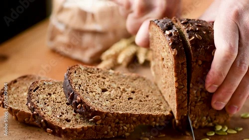 Person slicing fresh rye bread with seeds on cutting board. Closeup view photo