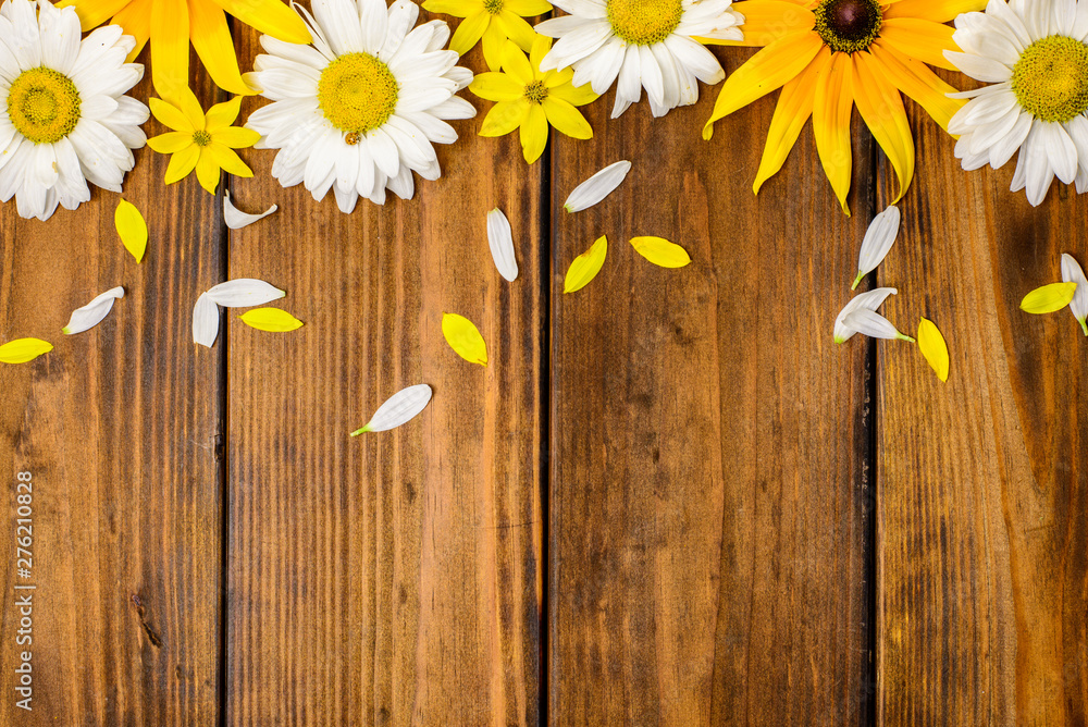 Obraz premium White daisies and garden flowers on a brown wooden table. Top view, copy space.