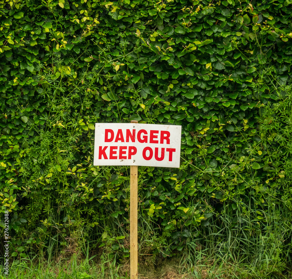 Danger Keep Out sign against a hedge