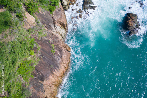 Aerial drone top view of ocean's beautiful waves crashing on the rocky island coast with green trees © stryjek