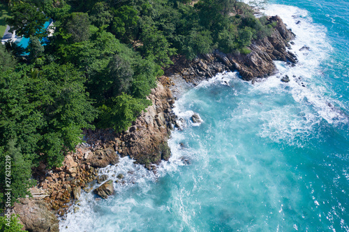 Aerial drone top view of ocean's beautiful waves crashing on the rocky island coast with green trees