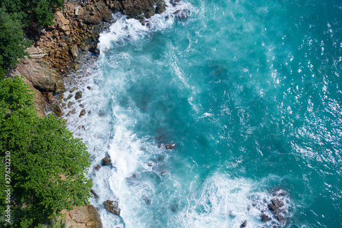 Aerial drone top view of ocean's beautiful waves crashing on the rocky island coast with green trees