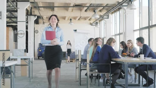 Business woman finishes the meeting, says goodbye to her colleagues, gets up from the table and leaves the office space. Coworking. Office life in the background