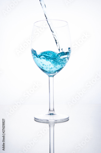 Blue cocktail is poured into a glass on a white background with reflection, splashes and bubbles