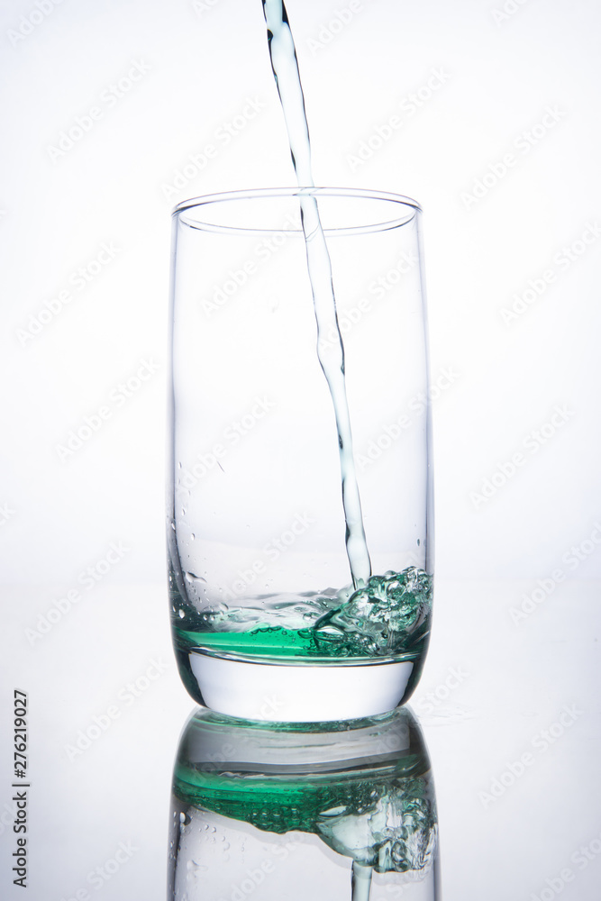 Green cocktail is poured into a glass on a white background with reflection, splashes and bubbles Green cocktail is poured into a glass on a white background with reflection, splashes and bubbles
