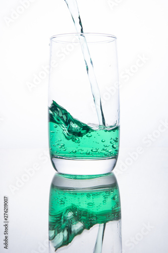 Green cocktail is poured into a glass on a white background with reflection, splashes and bubbles