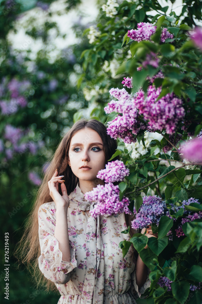 Fototapeta premium Beautiful big-eyed girl near the lilac tree.