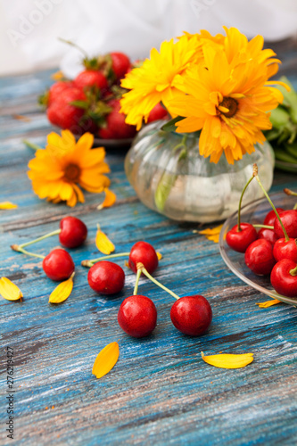 Summer on a wooden table: sweet cherry, green peas in the pods, strawberries, flowers