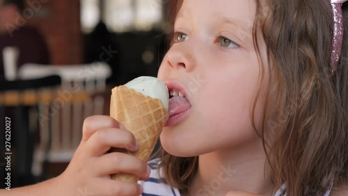 Little kid girl closeup portrait face eating licking ice cream cone with pleasure