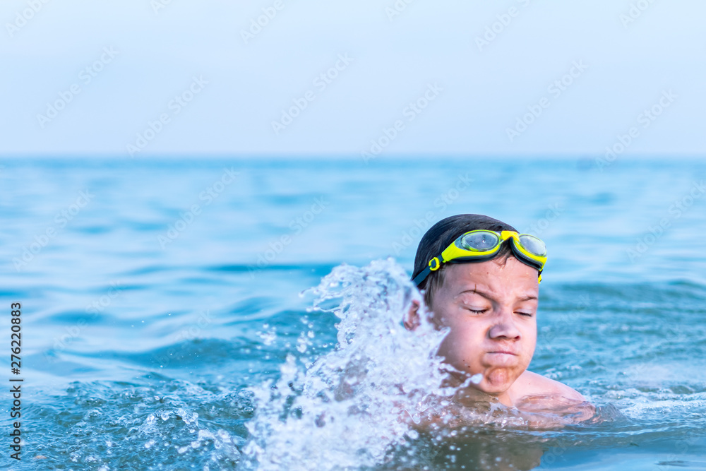 A 10-year-old boy swims in the sea at dawn with glasses for swimming.