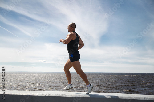 Athletic man doing jogging on the waterfront on a summer day.