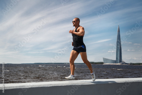 Athletic man doing jogging on the waterfront on a summer day.