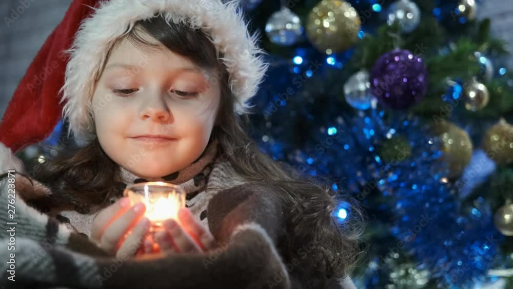 Girl in a blanket. Child with candles for Christmas. A charming little girl in a santaclaus hat holds a burning candle in her hands. Girl in a blanket. Child with candles for Christmas. A charming little girl in a santaclaus hat holds a burning candle in her hands.