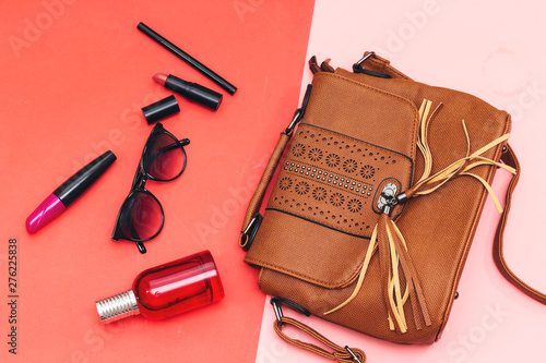 lipstick and mascara brush, bottle perfume and sunglasses and eyeliner and shoulder bag on pink and red paper