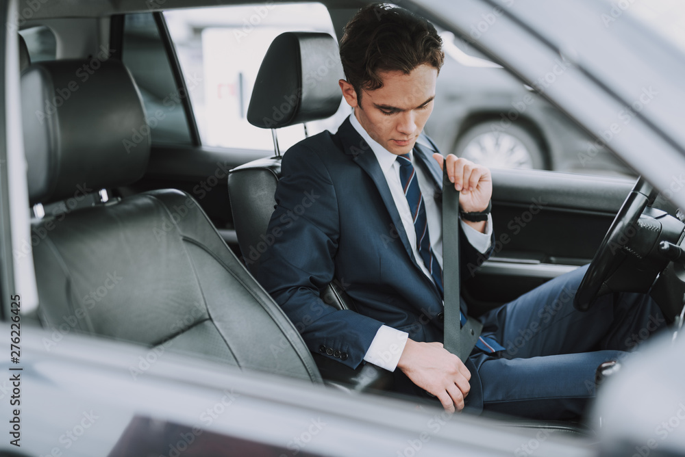 Young man in black suit using seat belt in his auto