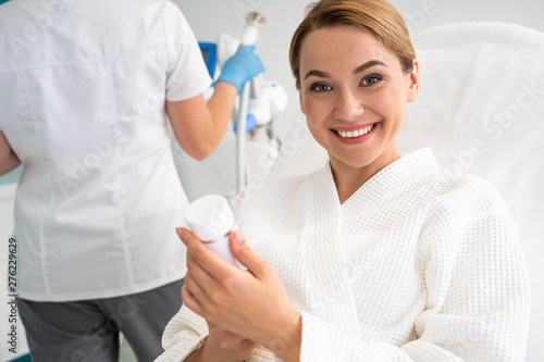 Excited woman with cosmetic bottle smiling to the camera