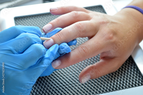 Manicurist in blue gloves smooths cuticle with orange stick