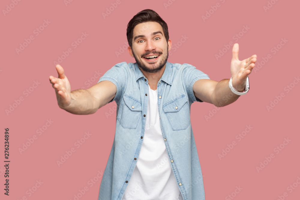 Portrait of happy handsome bearded young man in blue casual style shirt standing with raised arms, want to hug and looking at camera with toothy smile. indoor studio shot, isolated on pink background. Portrait of happy handsome bearded young man in blue casual style shirt standing with raised arms, want to hug and looking at camera with toothy smile. indoor studio shot, isolated on pink background.