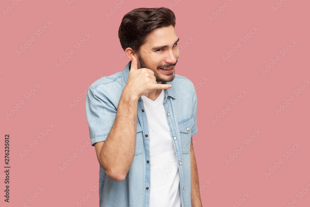 Call me. Portrait of happy handsome bearded young man in blue casual style shirt standing with call gesture hand on ear and looking at camera. indoor studio shot, isolated on pink background. Call me. Portrait of happy handsome bearded young man in blue casual style shirt standing with call gesture hand on ear and looking at camera. indoor studio shot, isolated on pink background.