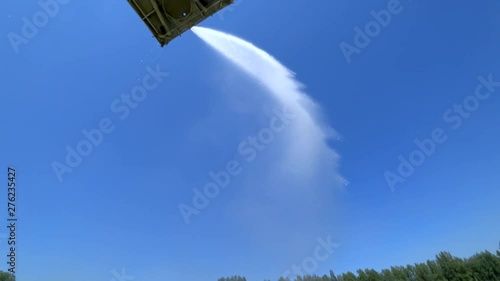 Water cannon (firefighter gun) sprays a stream of water from a platform in the air. Background - blue sky without clouds. Sun glare. Bottom view. Green Forest. photo