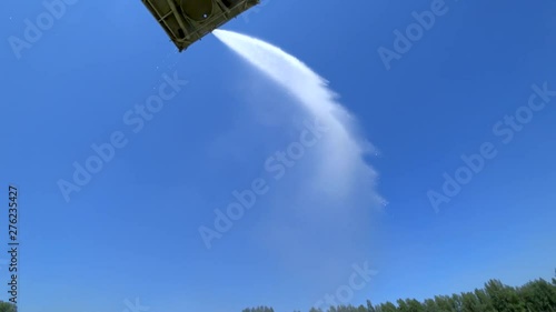 Water cannon (firefighter gun) sprays a stream of water from a platform in the air. Background - blue sky without clouds. Sun glare. Bottom view. Green Forest.