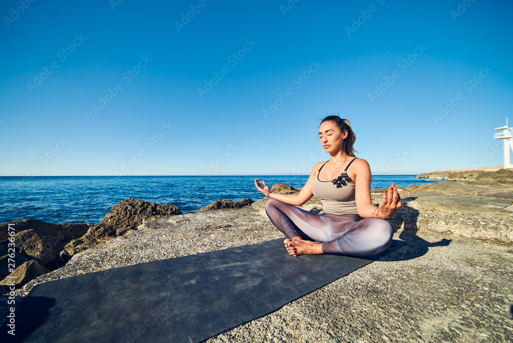 Calm young woman meditating at the beach against a beautiful blue sea.