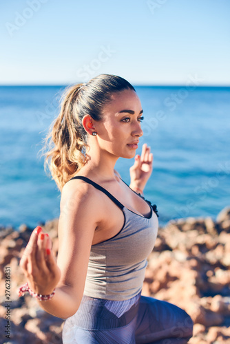 Portrait of beautiful young woman practicing yoga on seaside against blue sea.