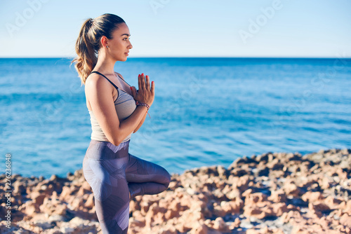 Fototapeta Naklejka Na Ścianę i Meble -  Beautiful young woman practicing yoga on seaside against blue sea.