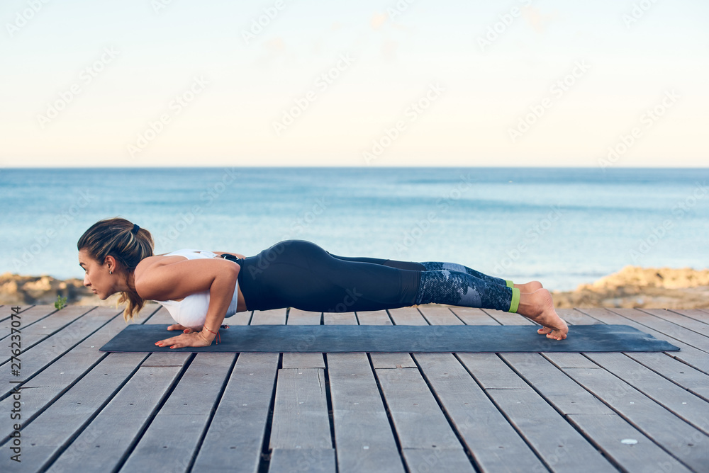 Beautiful young woman practicing yoga on seaside against blue sea.