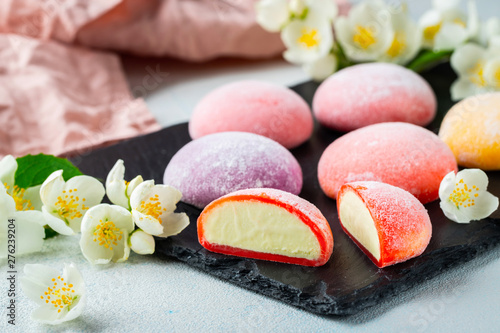 Multi-colored Japanese ice cream Mochi in rice dough and Jasmine flowers on a concrete blue background. Traditional Japanese dessert on a black slate photo