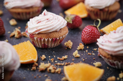 Orange cupcakes with strawberry filling and butter cream with fresh berries. Desserts on a dark background.