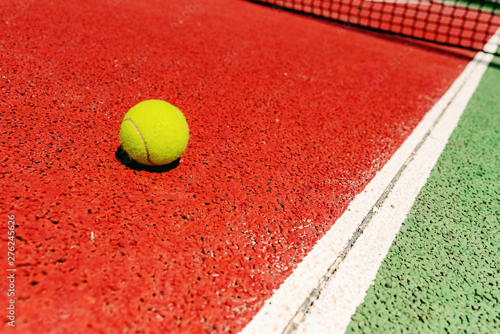 Yellow tennis ball on the red cement court to the sun, summer sports.