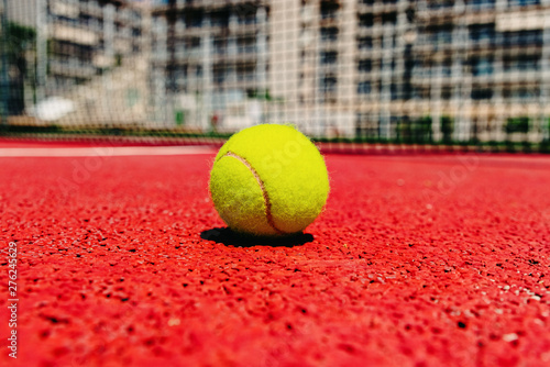 Yellow tennis ball on the red cement court to the sun, summer sports. © Joaquin Corbalan