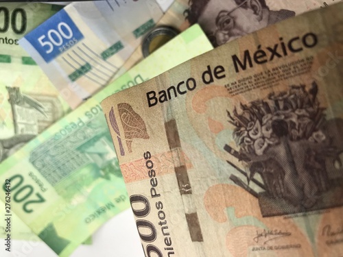 Many mixed Mexican peso bills spread over a wooden desk