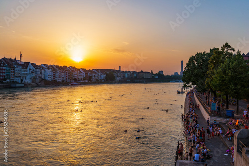 Top view from Middle Bridge of people relax and chill out on riverside, and swim and float on Rhine river during summer with background of  Cityscape and twilight sunset sky in Basel, Switzerland. photo