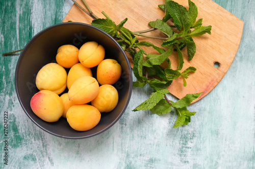Fresh fruits on green wooden background. Bowl of fresh sweet apricots and mint leaves. Top view.