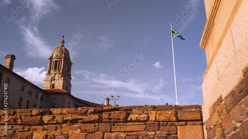 Slow motion: Clock tower and flag pole at Union Buildings stick out behind rugged sandstone wall. Slow motion slider movement photo