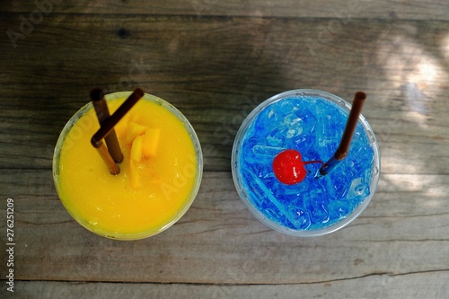 Refreshing Mango smoothie and blue hawaii italian soda with cherry on top on wooden table, top view.