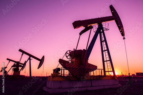 Oil pumps are running in the sunset at the oil field.