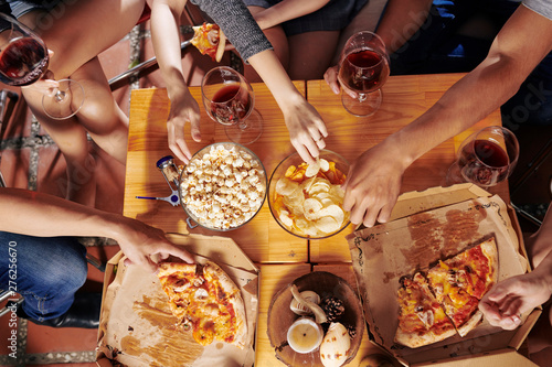 Hands of people eating pizza and snacks and drinking red wine at party, view from above