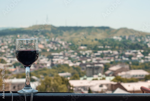 A glass of red wine with a view of the city  a glass on the balcony 
