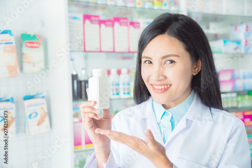 Smiling asian female pharmacist holding medicine and smile in pharmacy  chemist shop or drugstore 