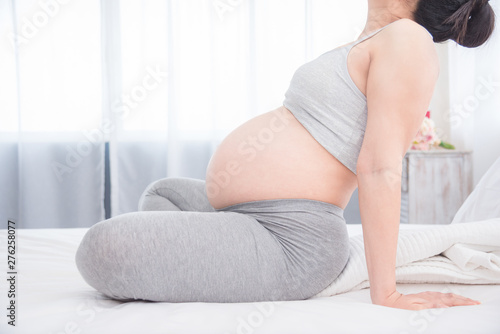 Pregnant woman sitting on bed and doing yoga for exercise. Pregnancy, maternity, preparation and expectation concept.