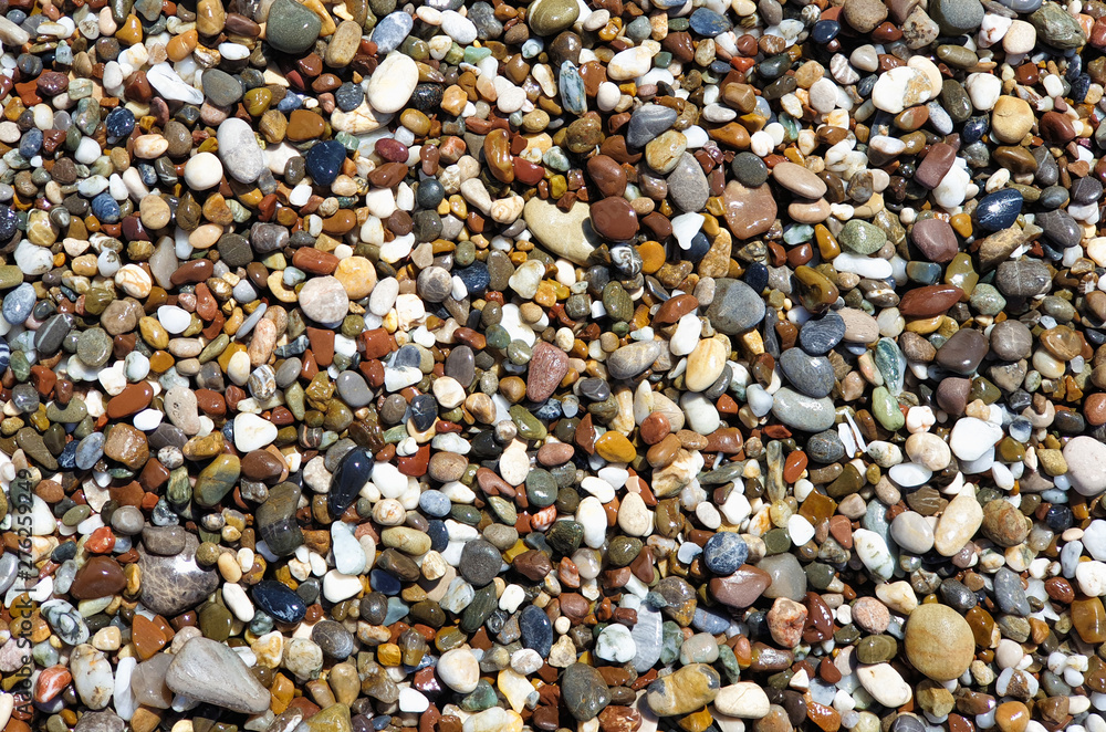 Multi-colored large sea pebbles of various shapes on the sandy shore of the Mediterranean sea for background