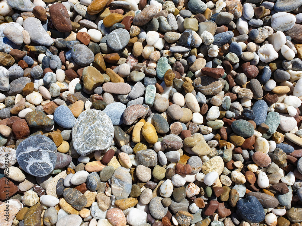 Multi-colored large sea pebbles of various shapes on the sandy shore of the Mediterranean sea for background Multi-colored large sea pebbles of various shapes on the sandy shore of the Mediterranean sea for background