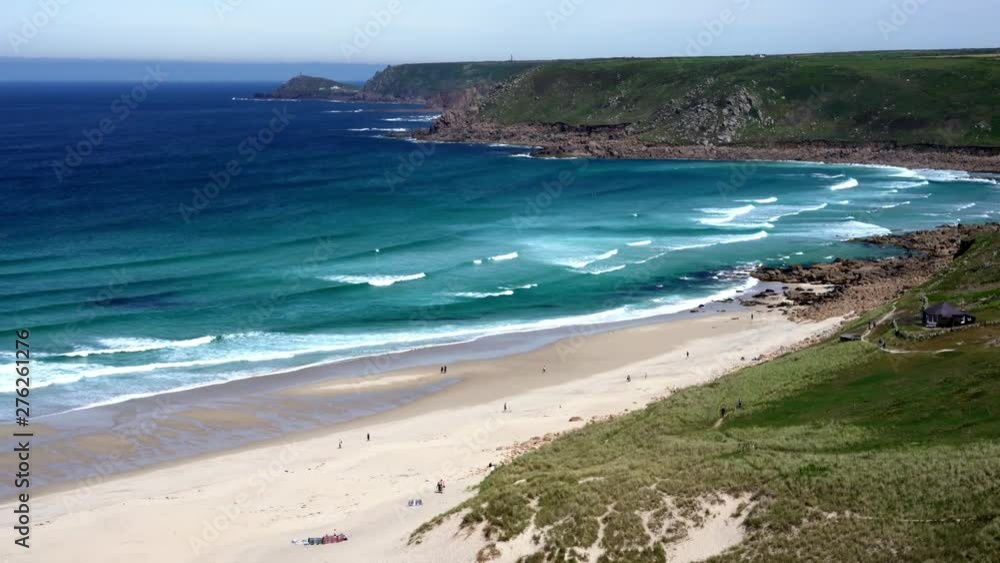 Ocean waves along the wide sandy shore at Sennen Cove in Cornwall with surfers and tourists walking on the beach. Zoom in 4k footage Ocean waves along the wide sandy shore at Sennen Cove in Cornwall with surfers and tourists walking on the beach. Zoom in 4k footage