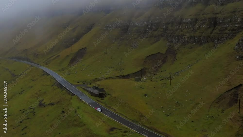 Aerial Car Parked on Side of Road in Green Valley with Rocky Face Rising Upwards, Suduroy Island, Faroe Islands Aerial Car Parked on Side of Road in Green Valley with Rocky Face Rising Upwards, Suduroy Island, Faroe Islands