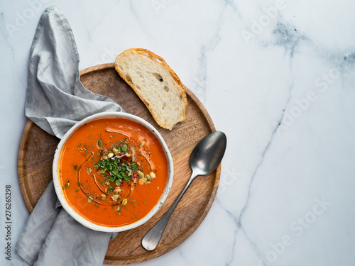 Gaspacho soup on round wooden tray over white marble tabletop. Bowl of traditional spanish cold soup puree gazpacho on light marble background. Copy space for text or design. Top view or flat lay.